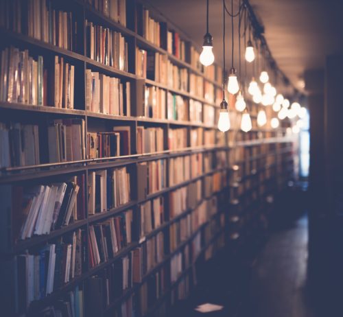 A dimly lit library aisle featuring rows of bookshelves filled with books on music theory, illuminated by hanging pendant lights that create a warm and inviting atmosphere.